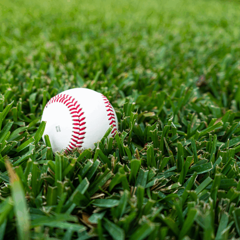A white baseball with red stitching resting on lush, green Raleigh St. Augustine grass